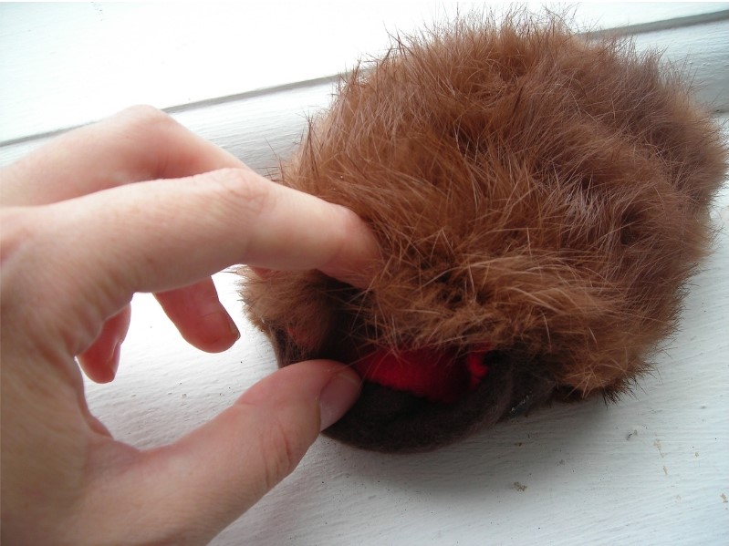 sculpture made of fur and fabric filled with dirt, my finger is touching a red opening on the creature's underbelly